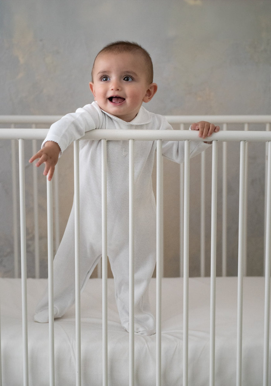 Baby in white Arubana outfit standing in crib